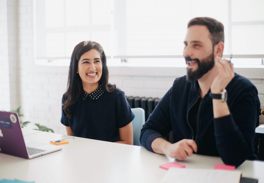 Woman and man discussing ideas in front of a laptop while smiling in a business meeting