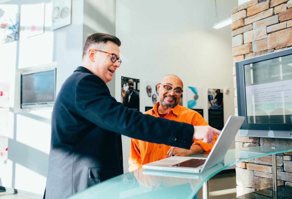 Two business people point and smile at a laptop that is in on a desk in front of them